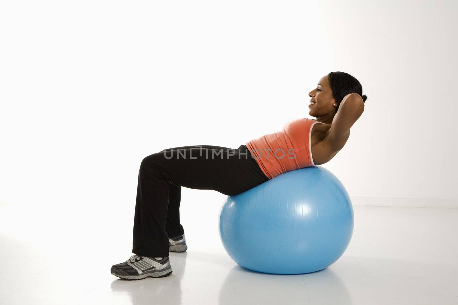 Side view of African American woman balancing on exercise ball doing crunches.