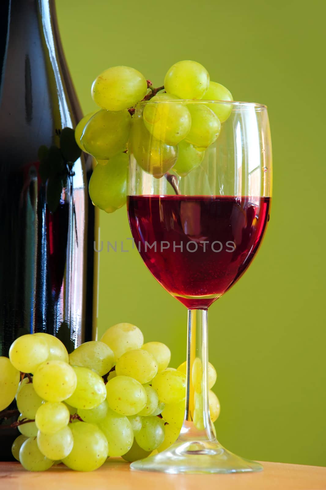 Red wine glass with grapes cluster and bottle over green