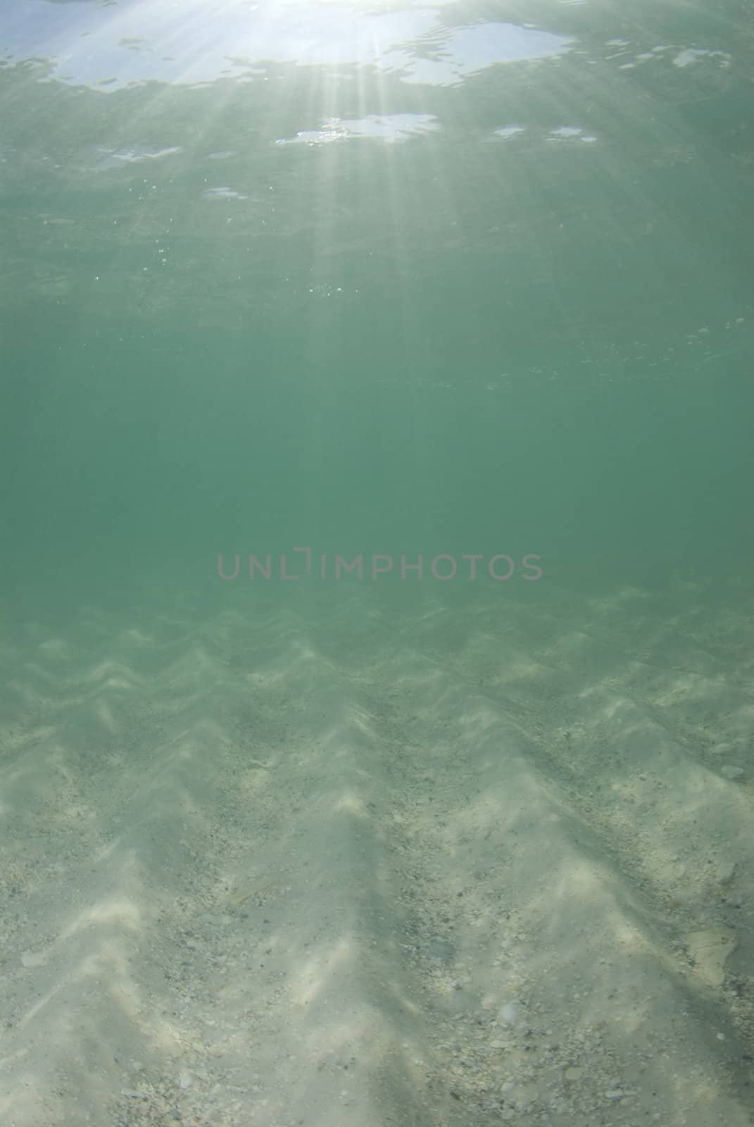 Underwater view of sunbeams stream through the surface of the ocean and dancing on the floor of the sea on a bright sunny day.  Bright sand and blue sky.
