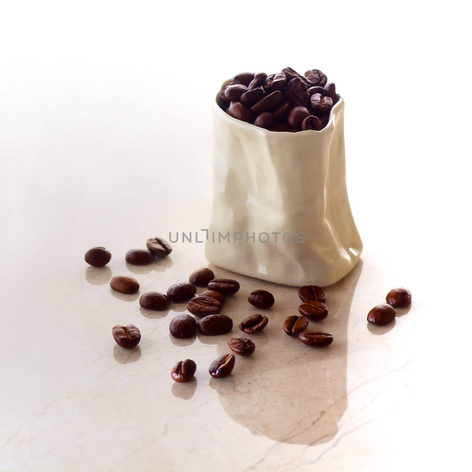 A ceramic bag filled with coffee beans spilling onto a marble surface in square format