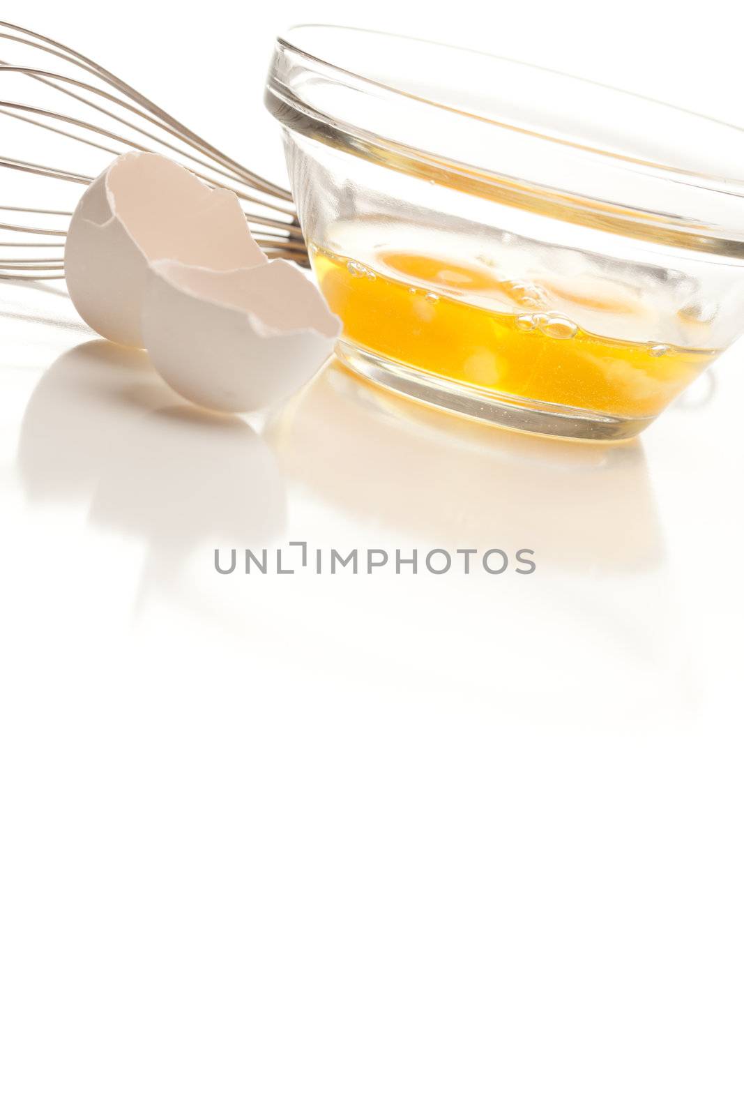 Hand Mixer with Eggs in a Glass Bowl on a Reflective White Background.