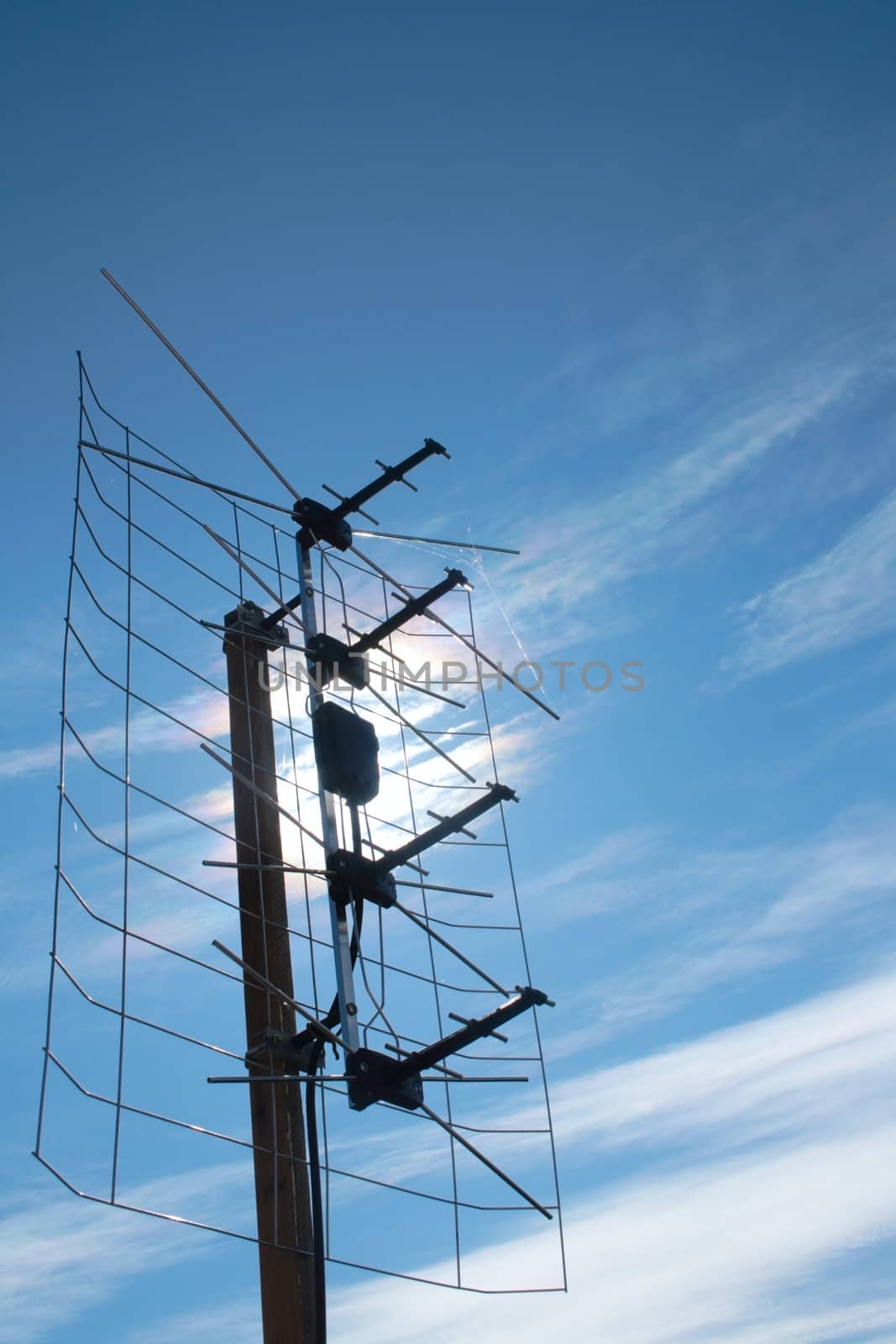 aerial TV antenna on rooftop over blue sky and sun