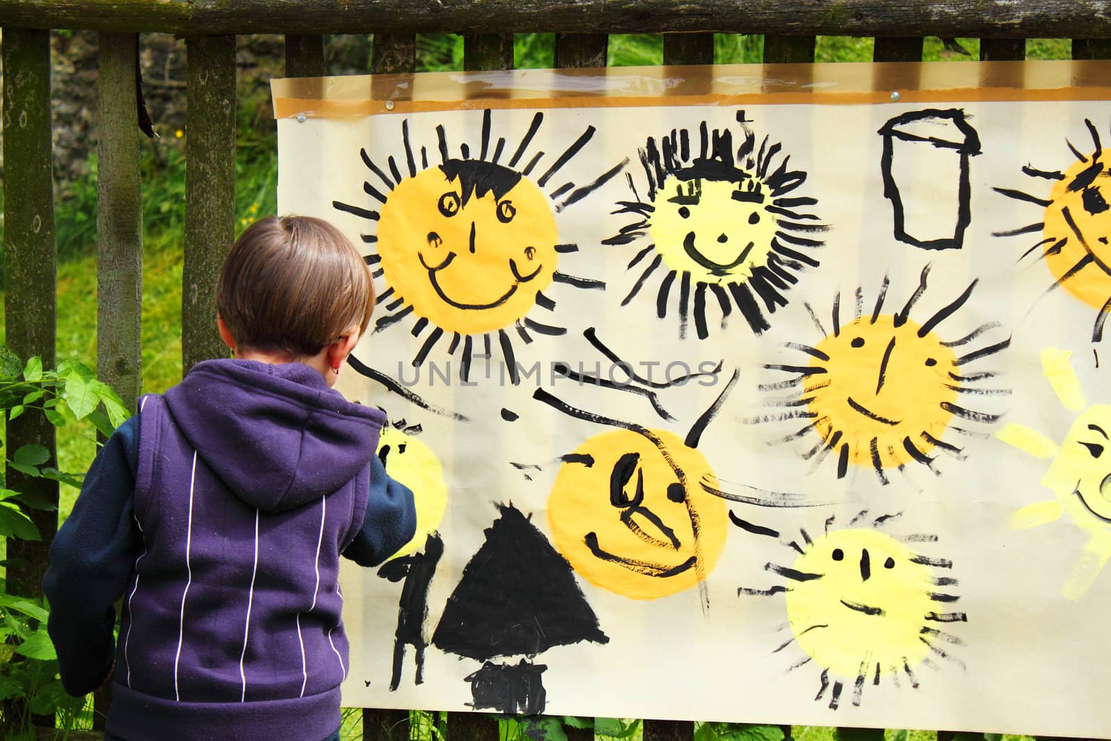 baby girl paints the sun on the big paper outdoor
