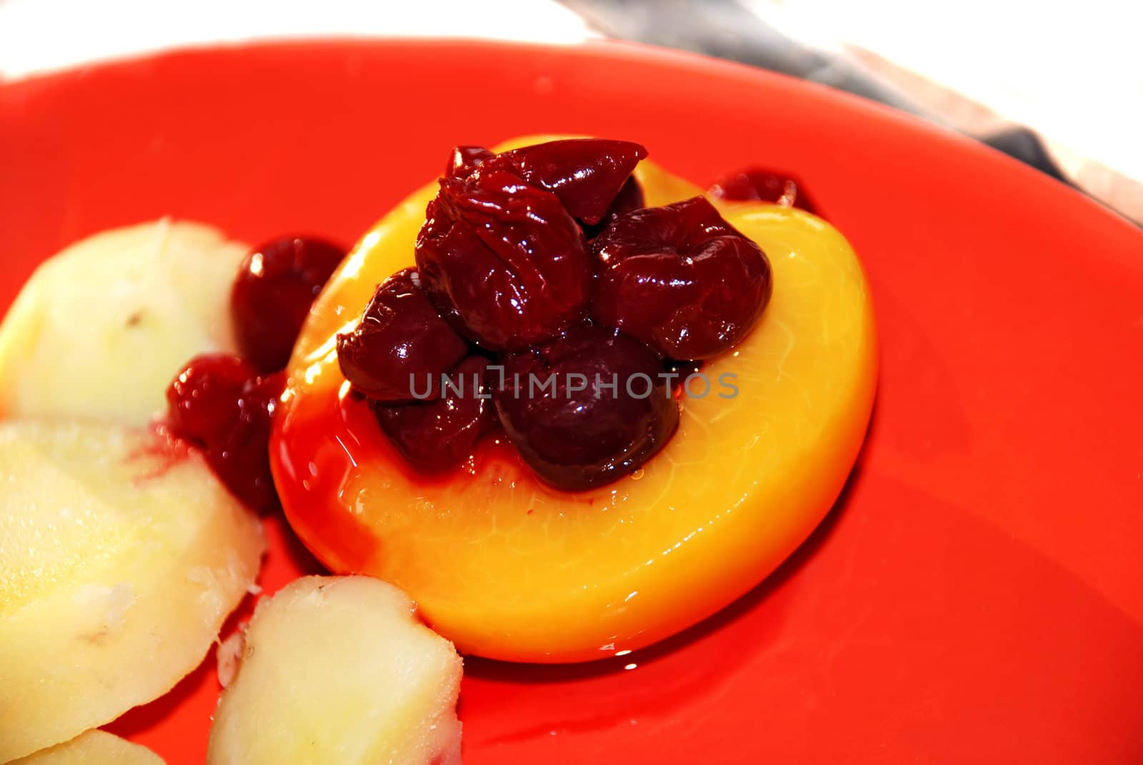 cherries and peach from fruit compote on red plate