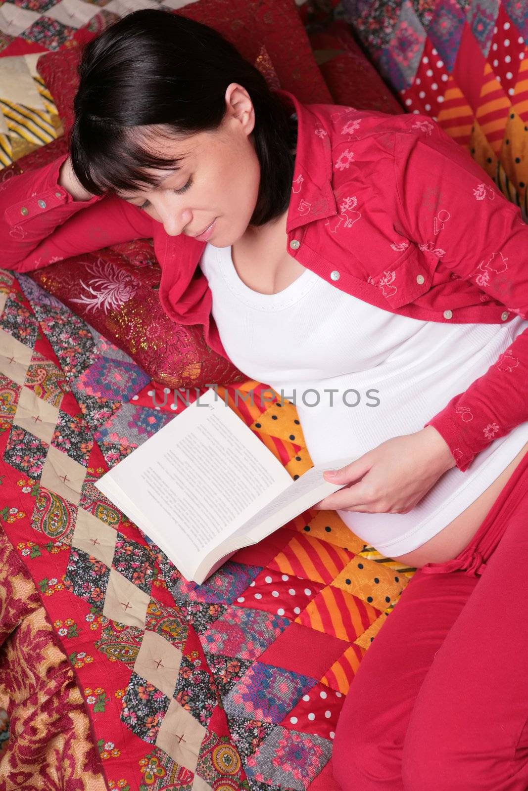 expectant mother smiles and reads book on the patchwork cover