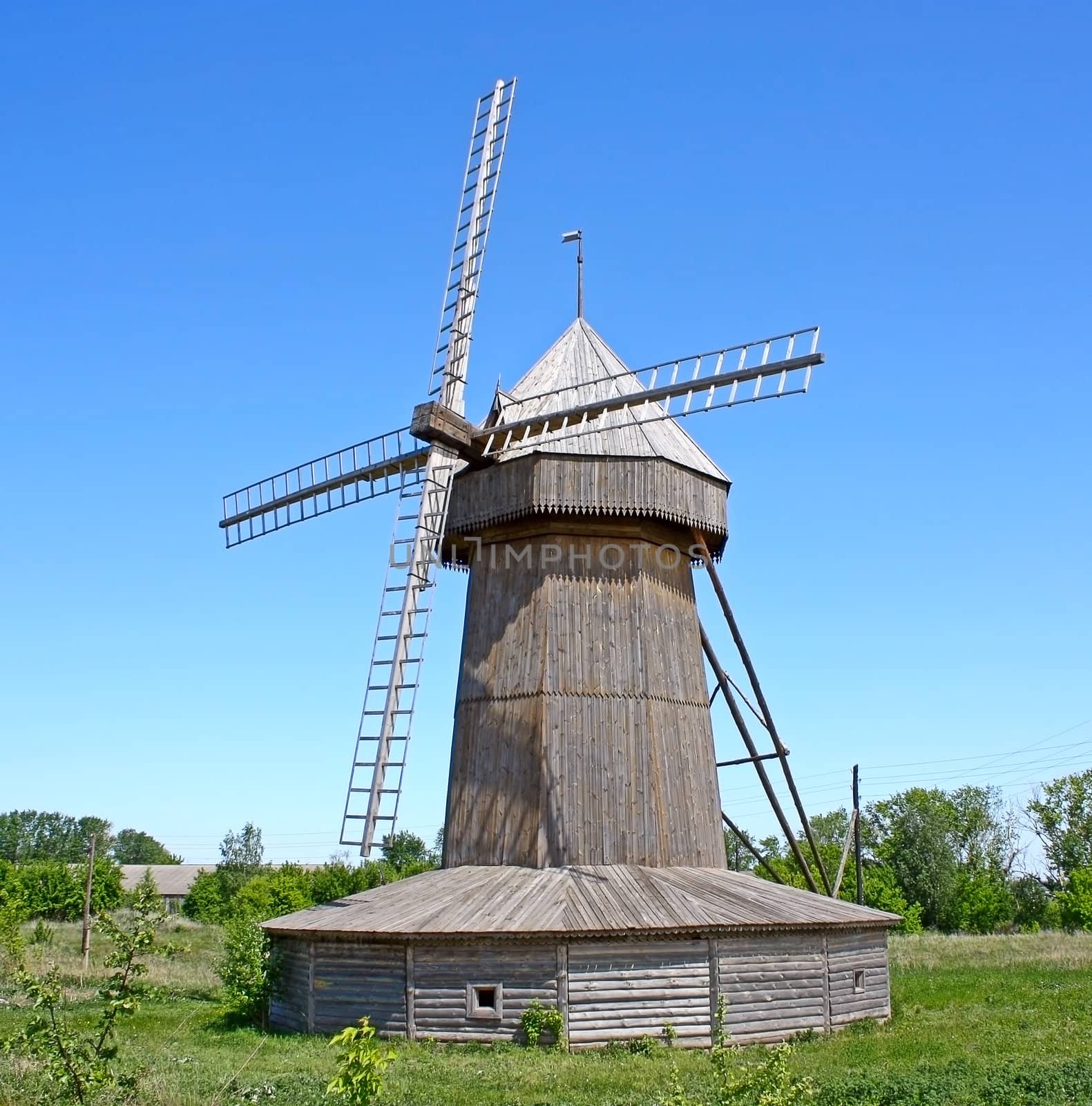 On the green grass, the wooden windmill against the blue sky.