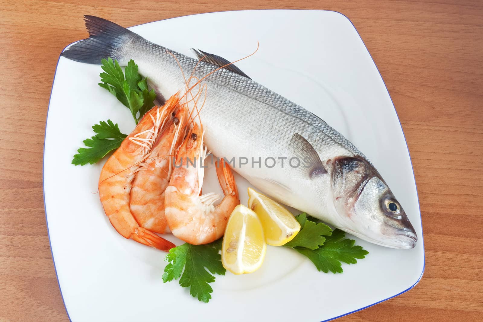 plate with sea bass, prawns, lemon and parsley isolated on wooden background
