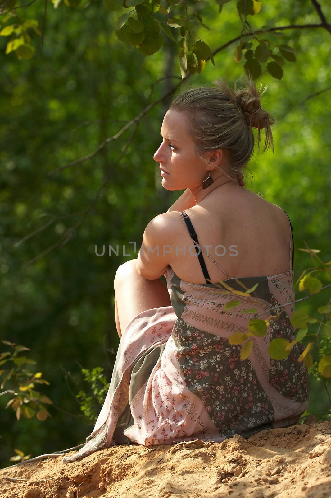 Beautiful woman sits among trees.  Lost in thought is contemplating the nature.