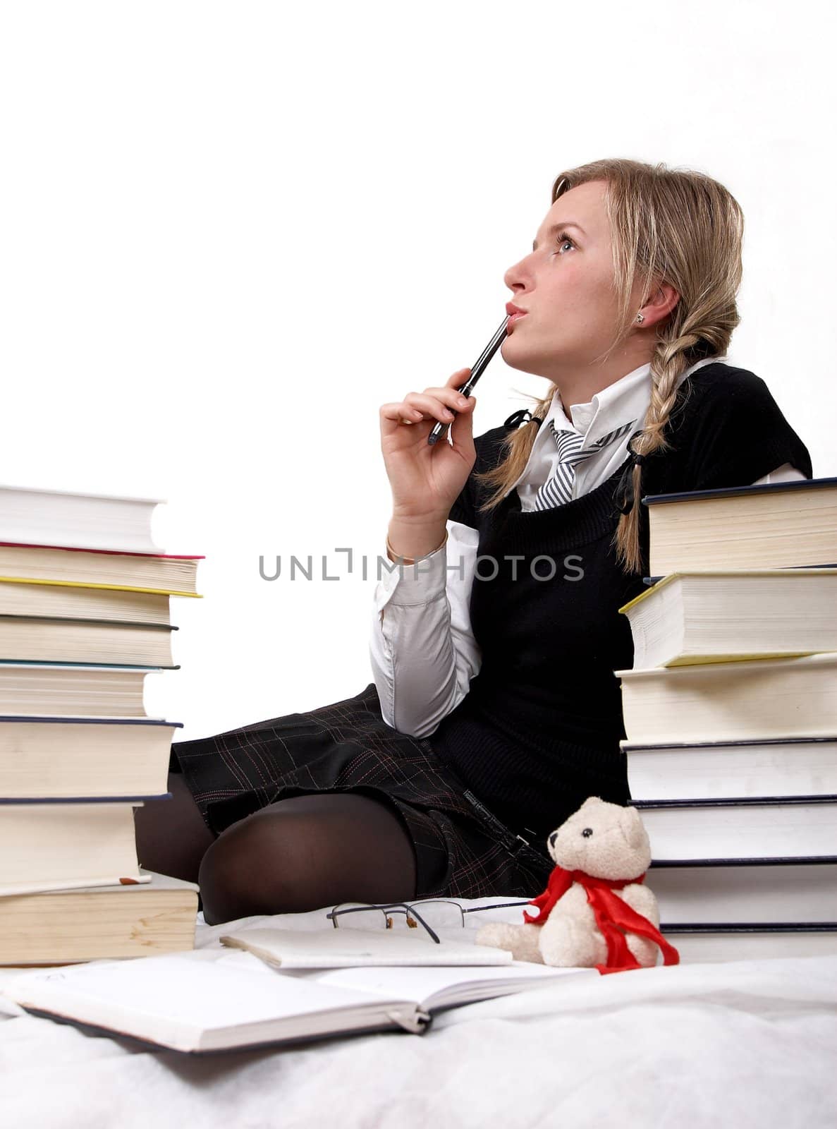 Schoolgirl or student is thinking. She is pensive, so is putting the ballpoint pen to the mouth. Isolated on white.