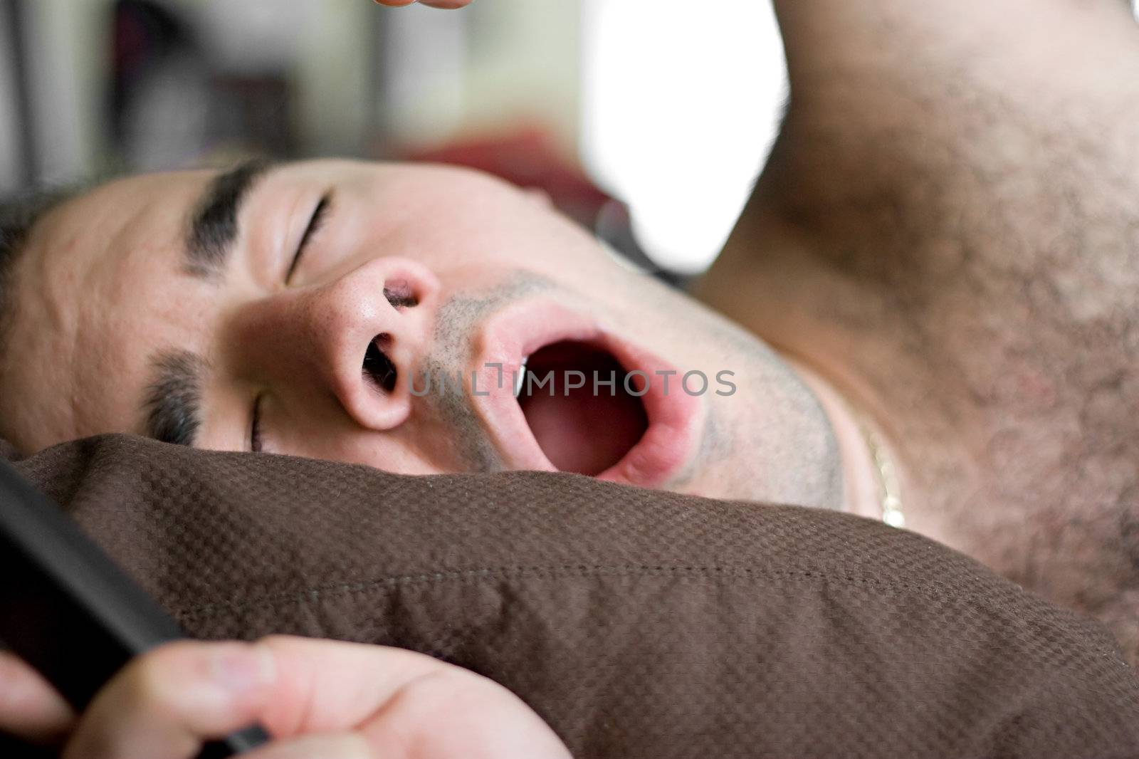 A young man is stretching and yawning in bed.