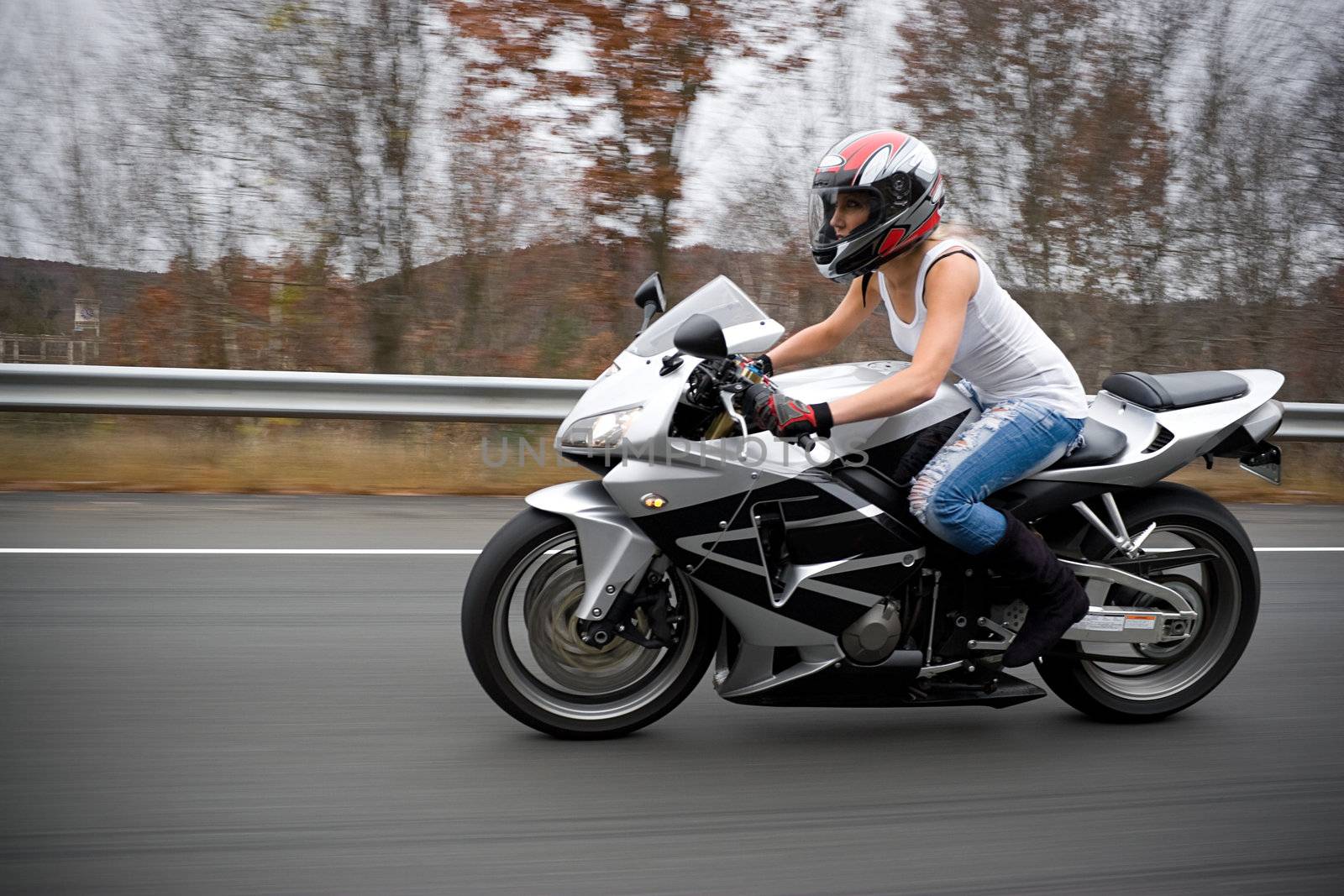 A pretty blonde girl in action driving a motorcycle at highway speeds.