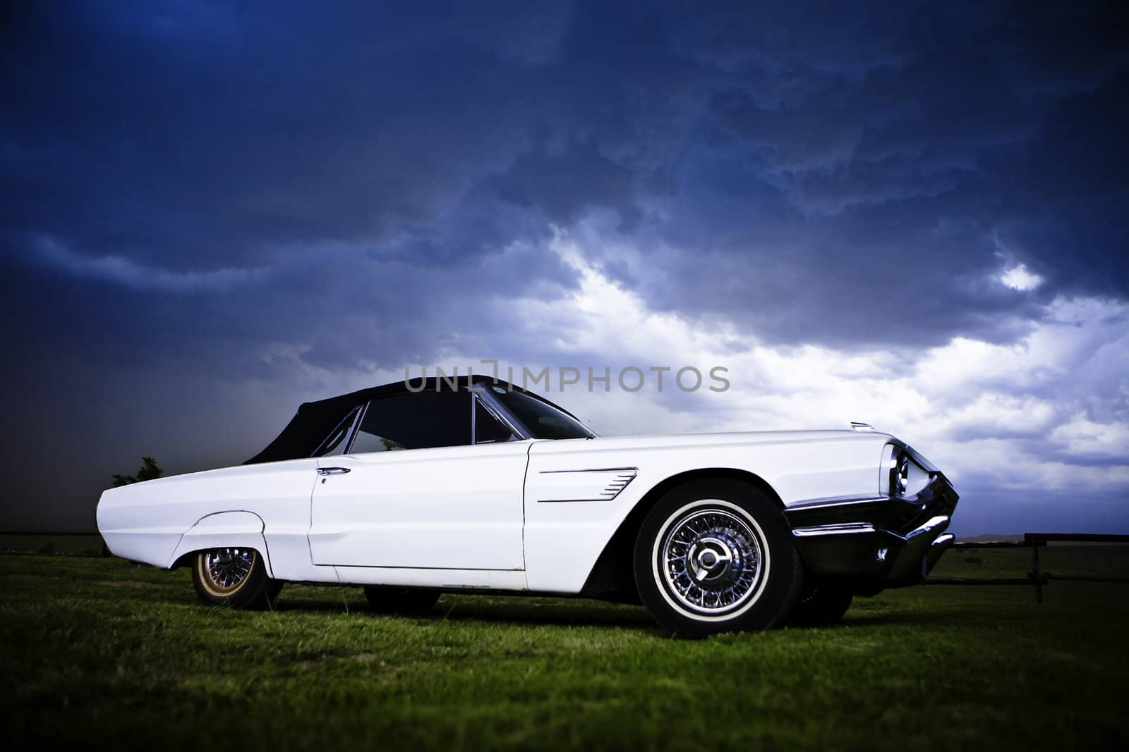 an old vintage convertible car on a green lawn against a dramatic cloudy sky