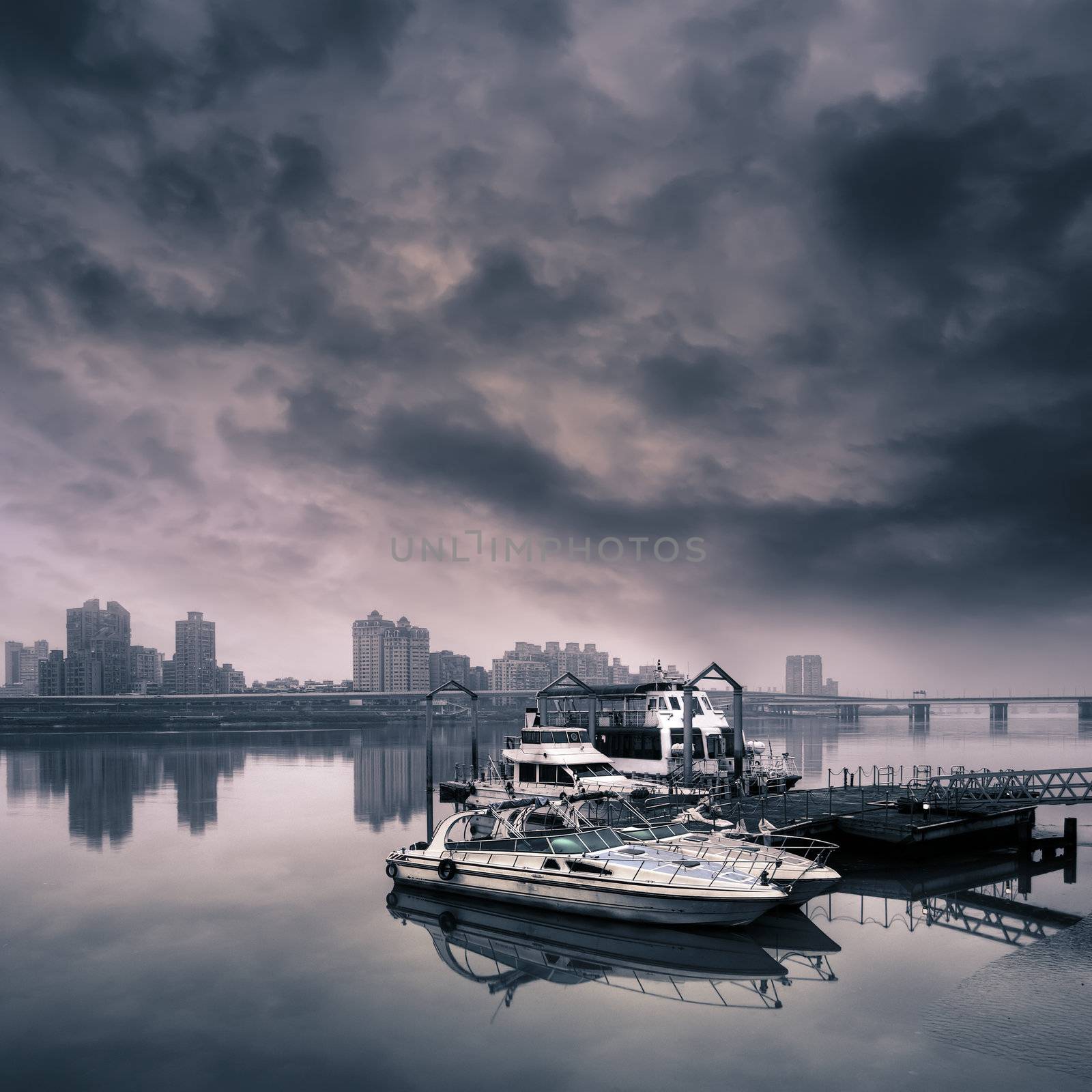 Cityscape of harbor with boat on water against dramatic sky.