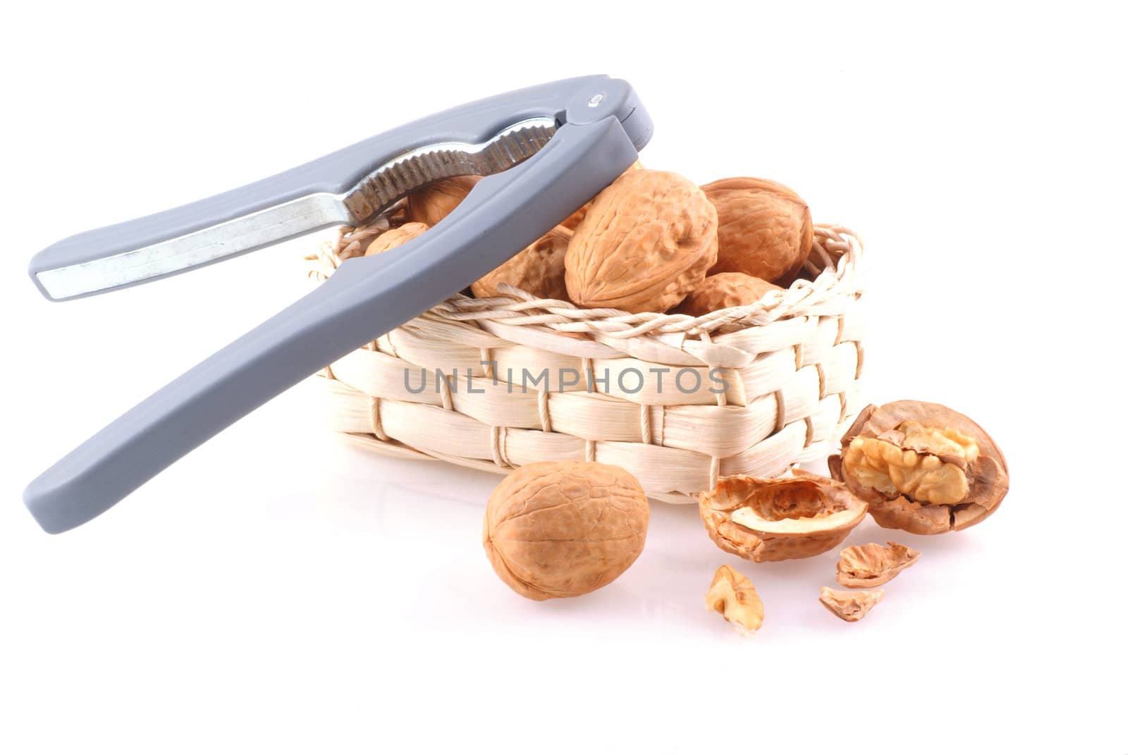 Basket full of walnuts with nutcracker, isolated on white.