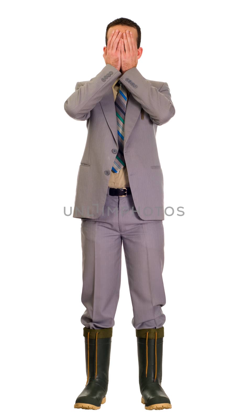 Full body view of an embarassed businessman wearing a grey suit and covering his face because he is wearing rubber boots