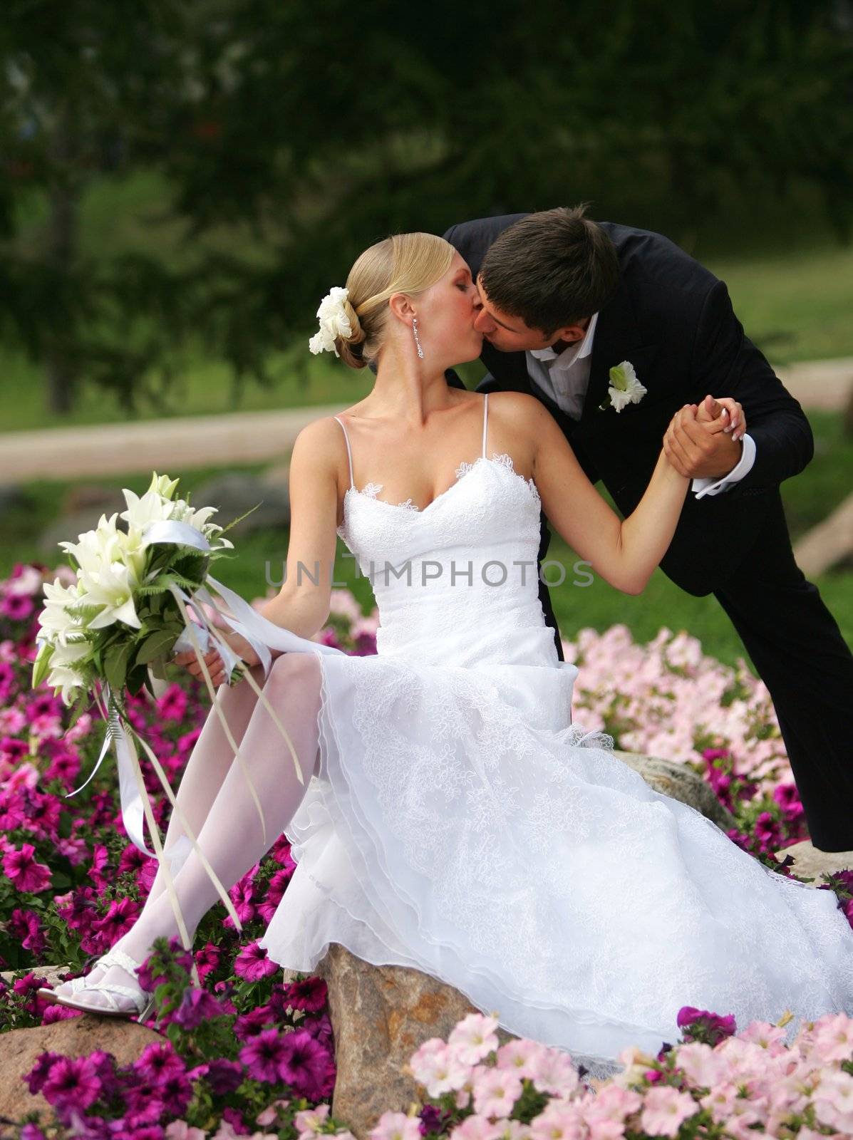 Newlywed couple kissing on flower bed in countryside.