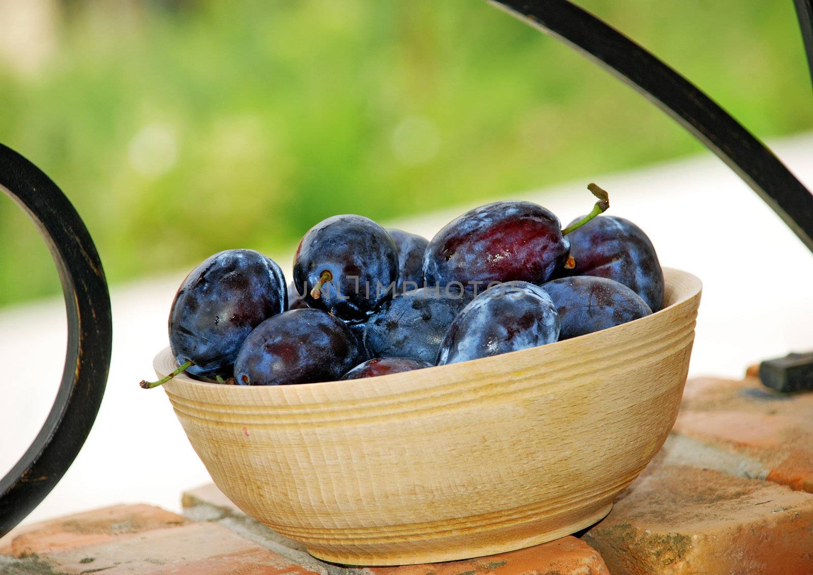 Blue ripe plums in wooden bowl over brick fence