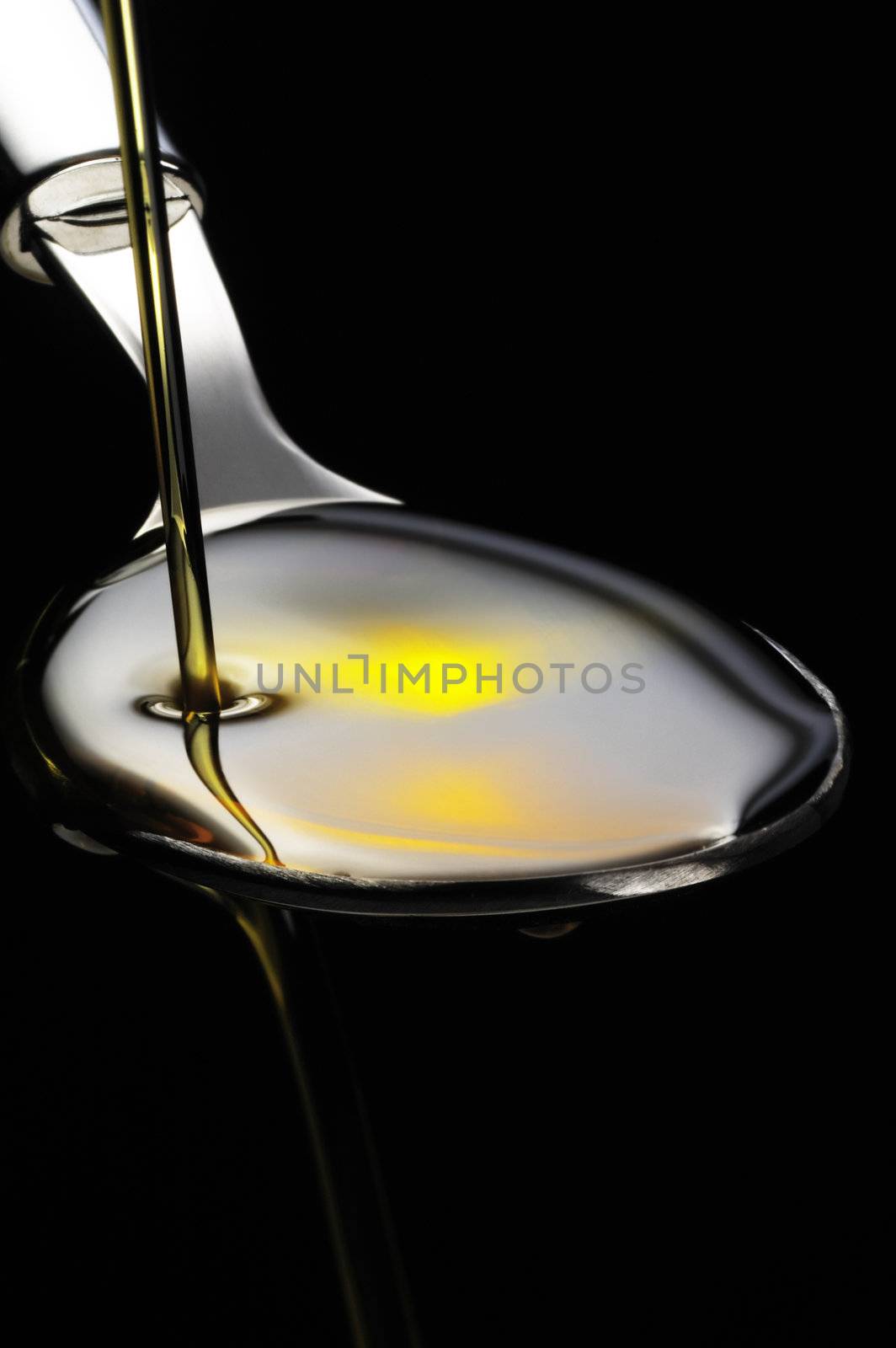 olive oil poured on a spoon over black background