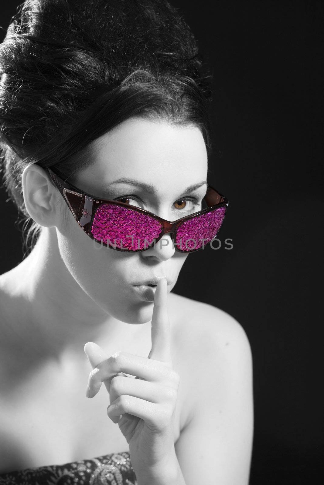 Cute brunette with pink sunglasses putting her finger to her lips