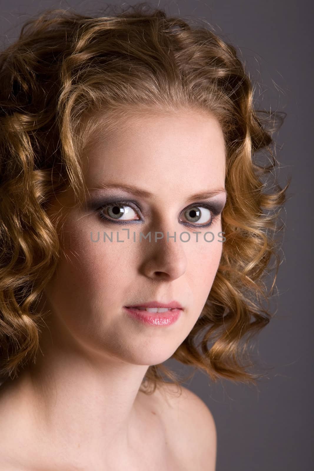 Beautiful young woman with curly blond hair on grey background