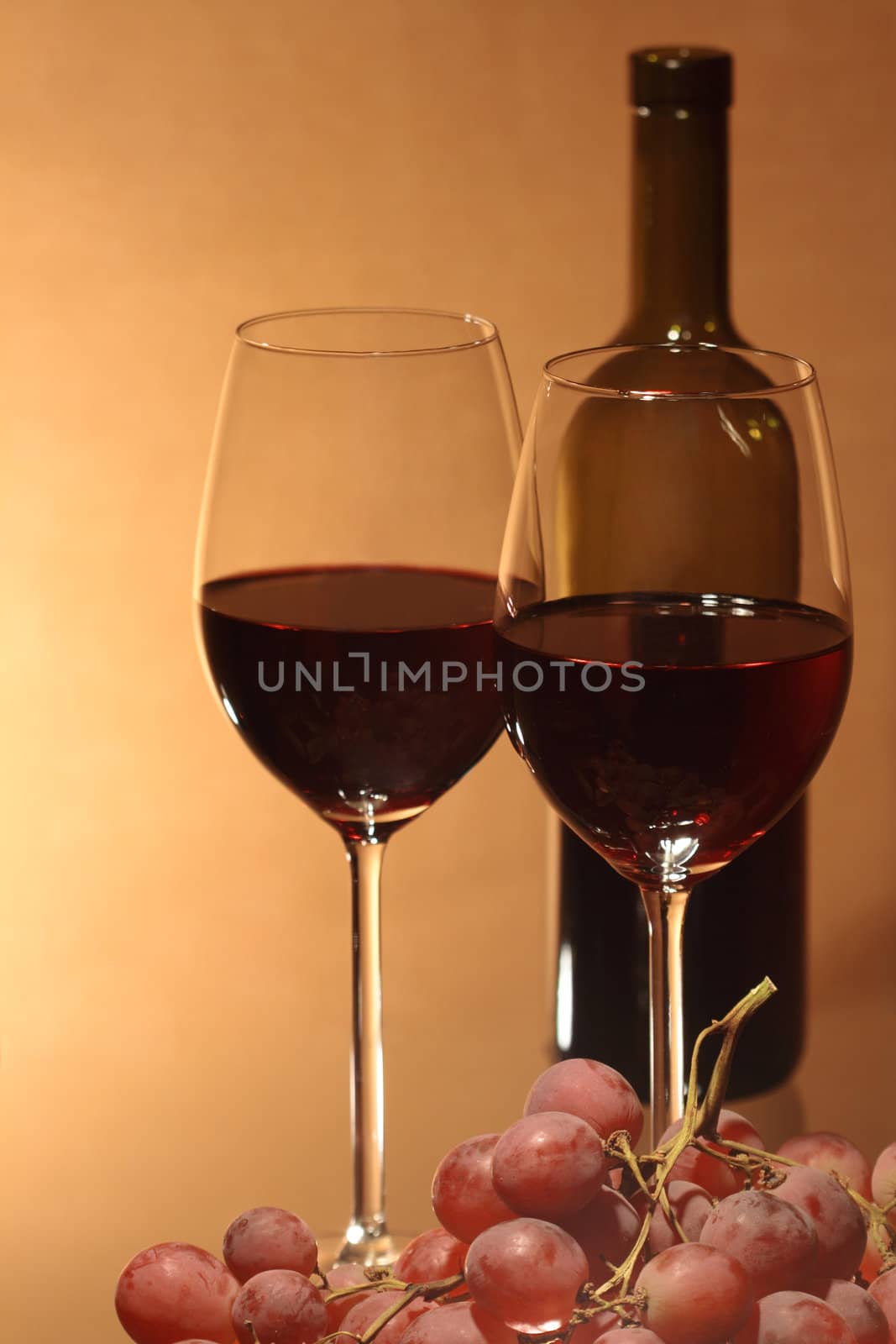 Grapes and two wineglasses near bottle of red wine on brown background