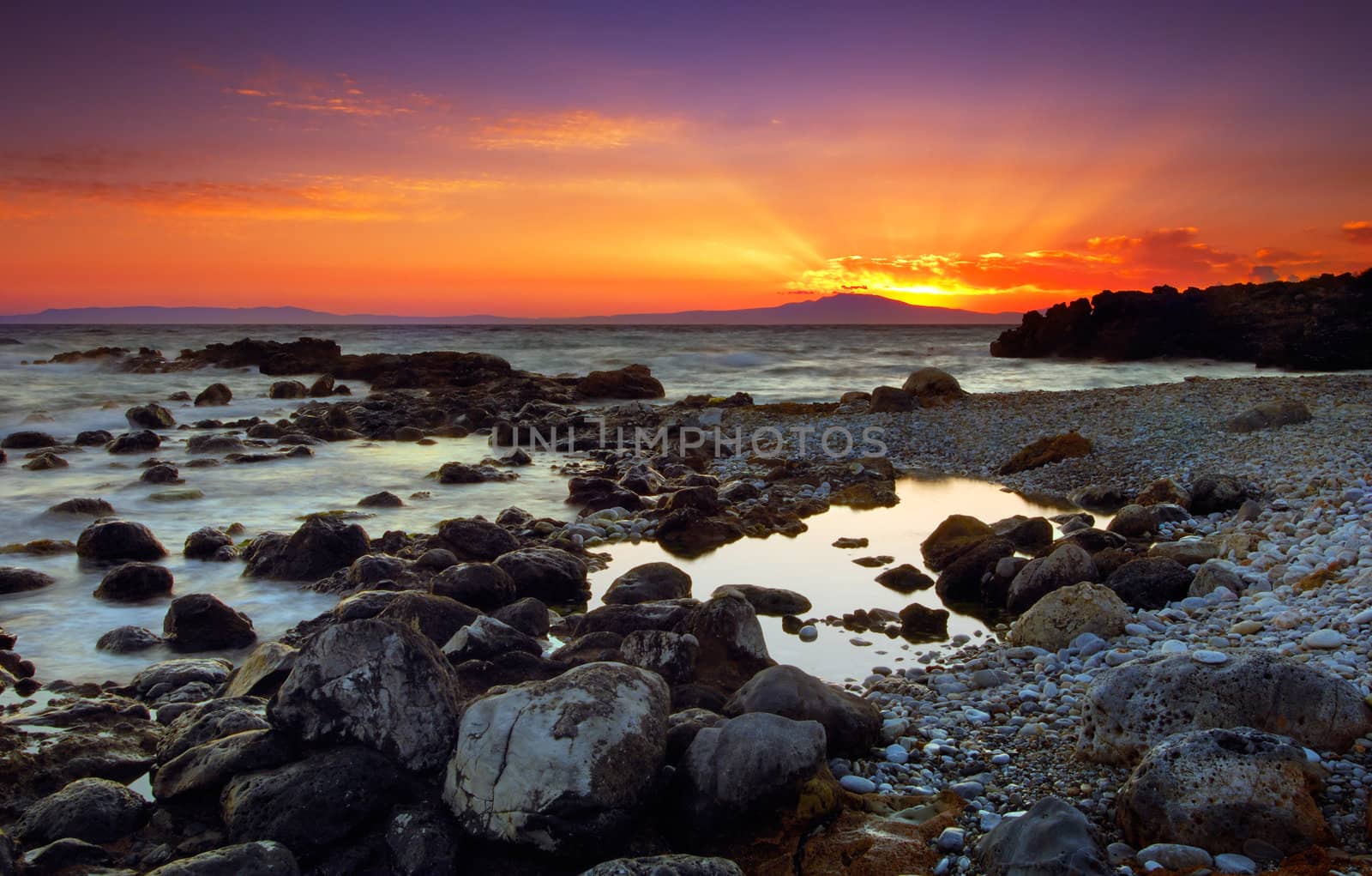 Image shows a spectacular sunset over a rocky seascape, in Mani peninsula, southern Greece