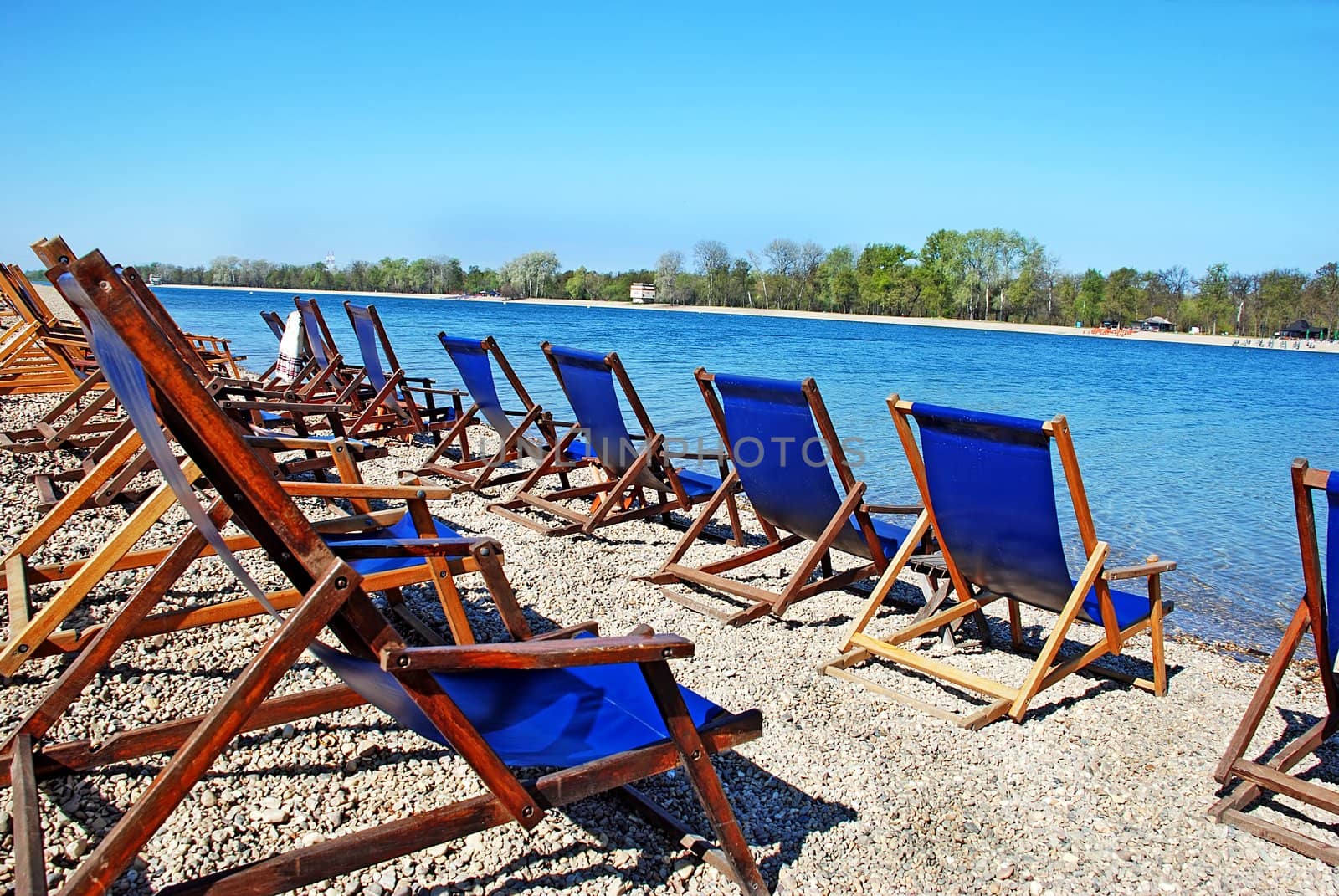 row of  folding chairs by on beach by blue water