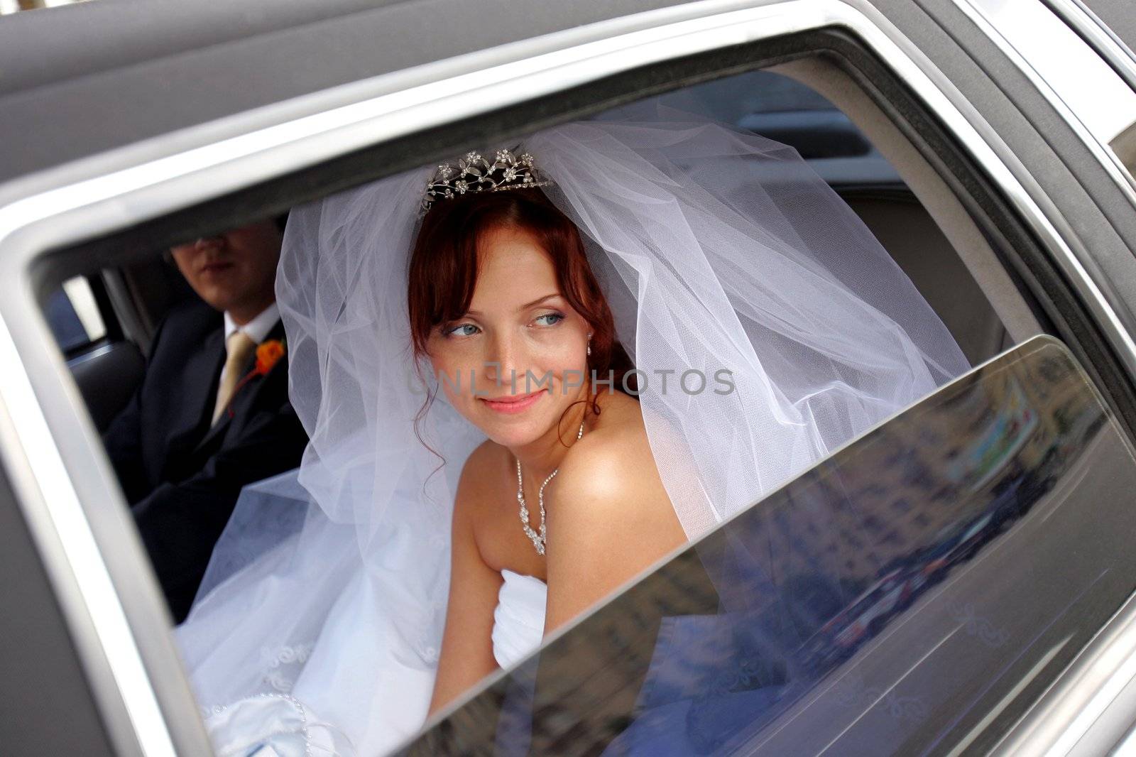 Smiling bride with groom in wedding car limousine.