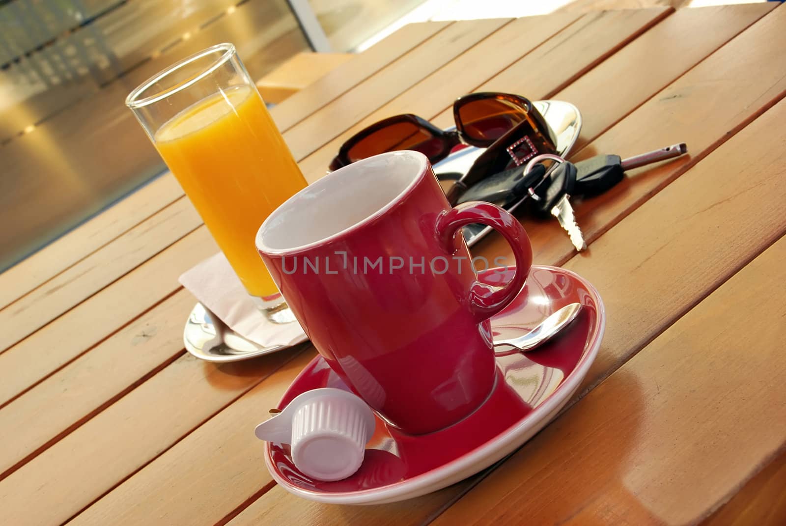 Red cup of coffee, juice, sunglasses and car key on table