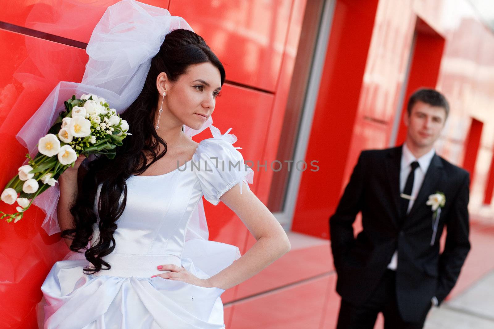 bride and groom by the red wall