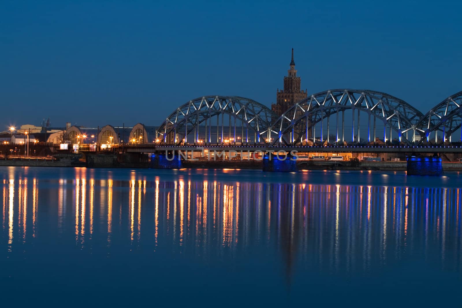 Railway bridge with reflection in river at night. Riga, Latvia.