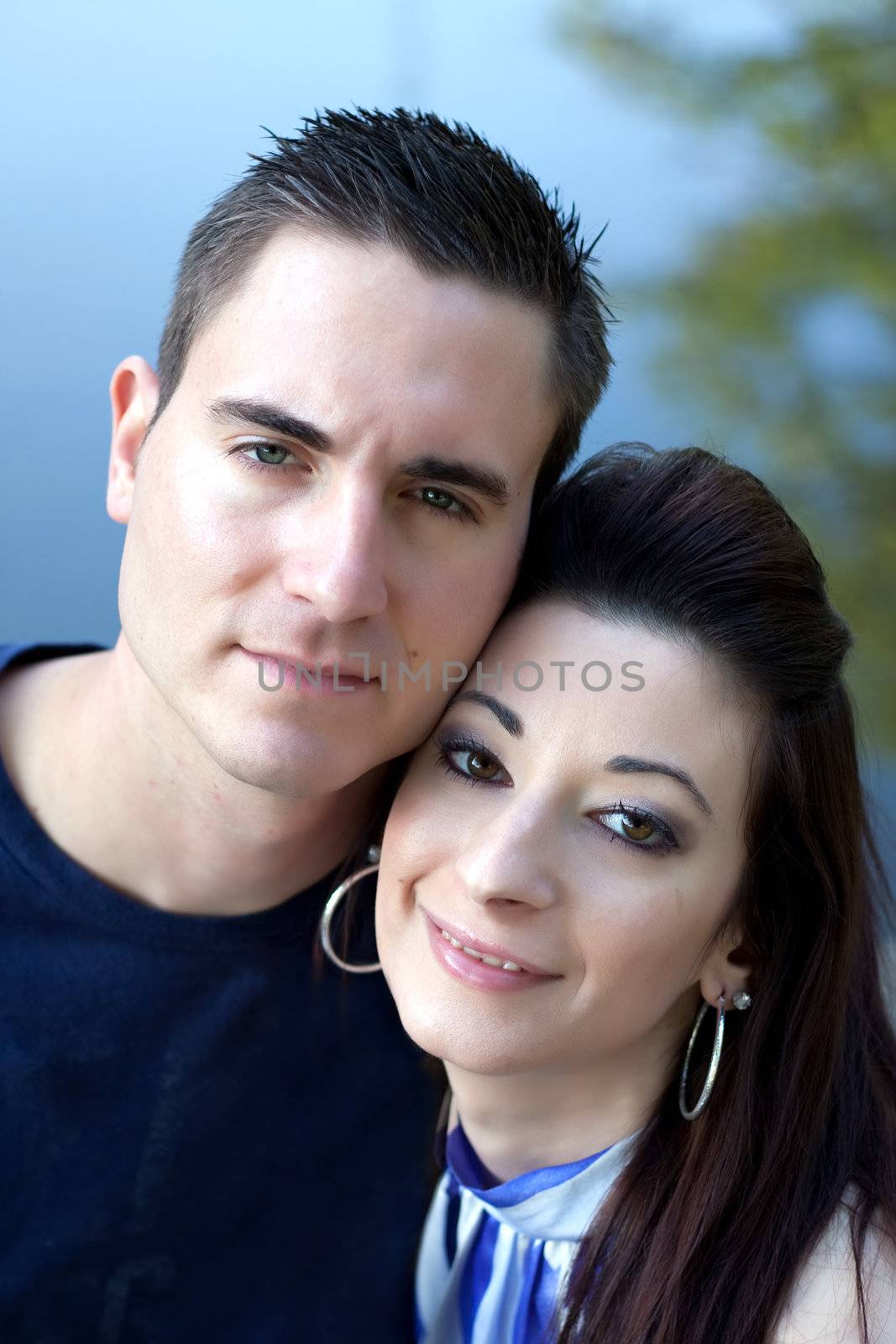 A happy young couple in their mid 20s smiling with their heads close together.