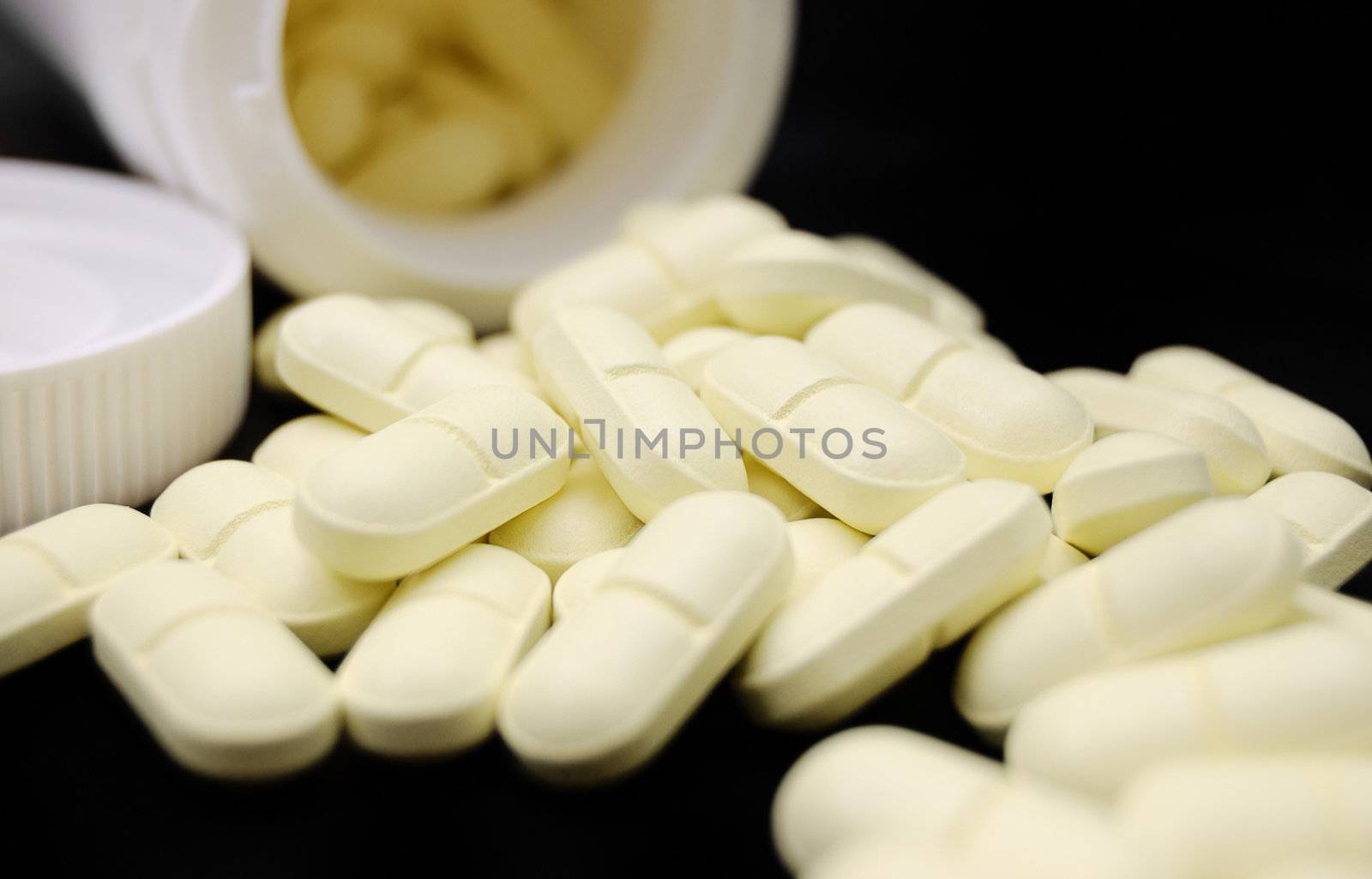 heap of pills and container on black (shallow DOF)