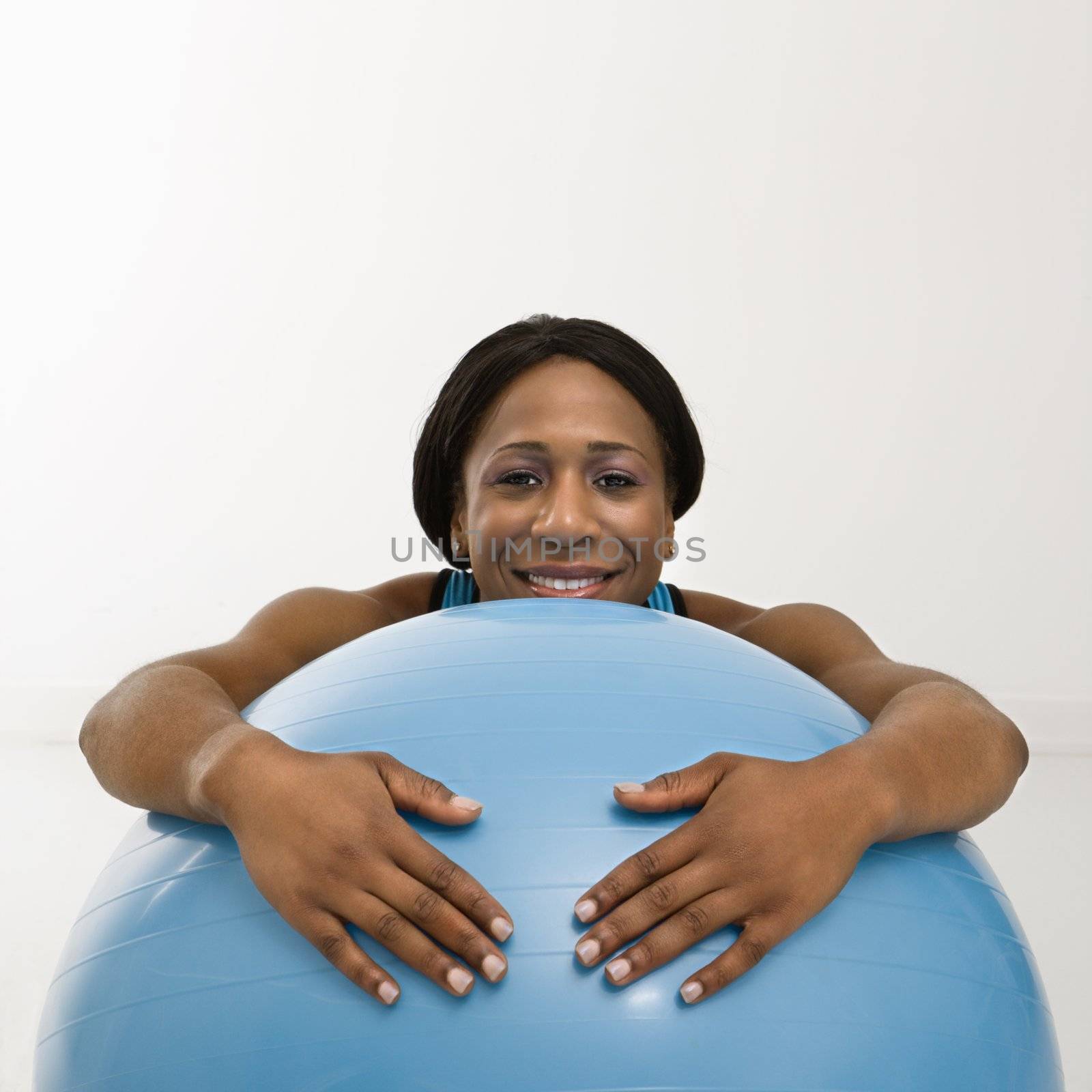 African American young adult woman resting with arms draped over exercise ball smiling at viewer.