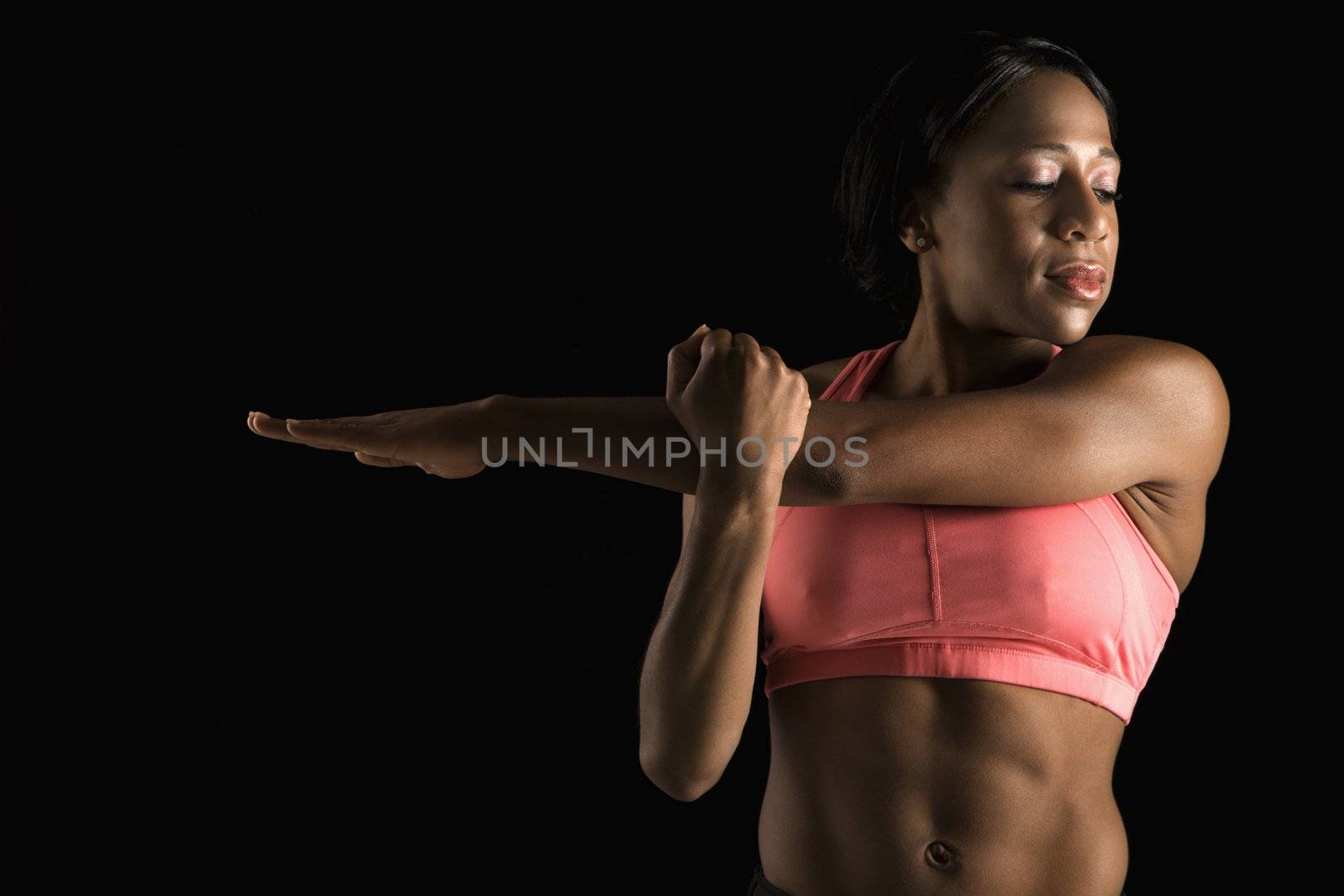 African American young adult woman in sports bra stretching arms with eyes closed.