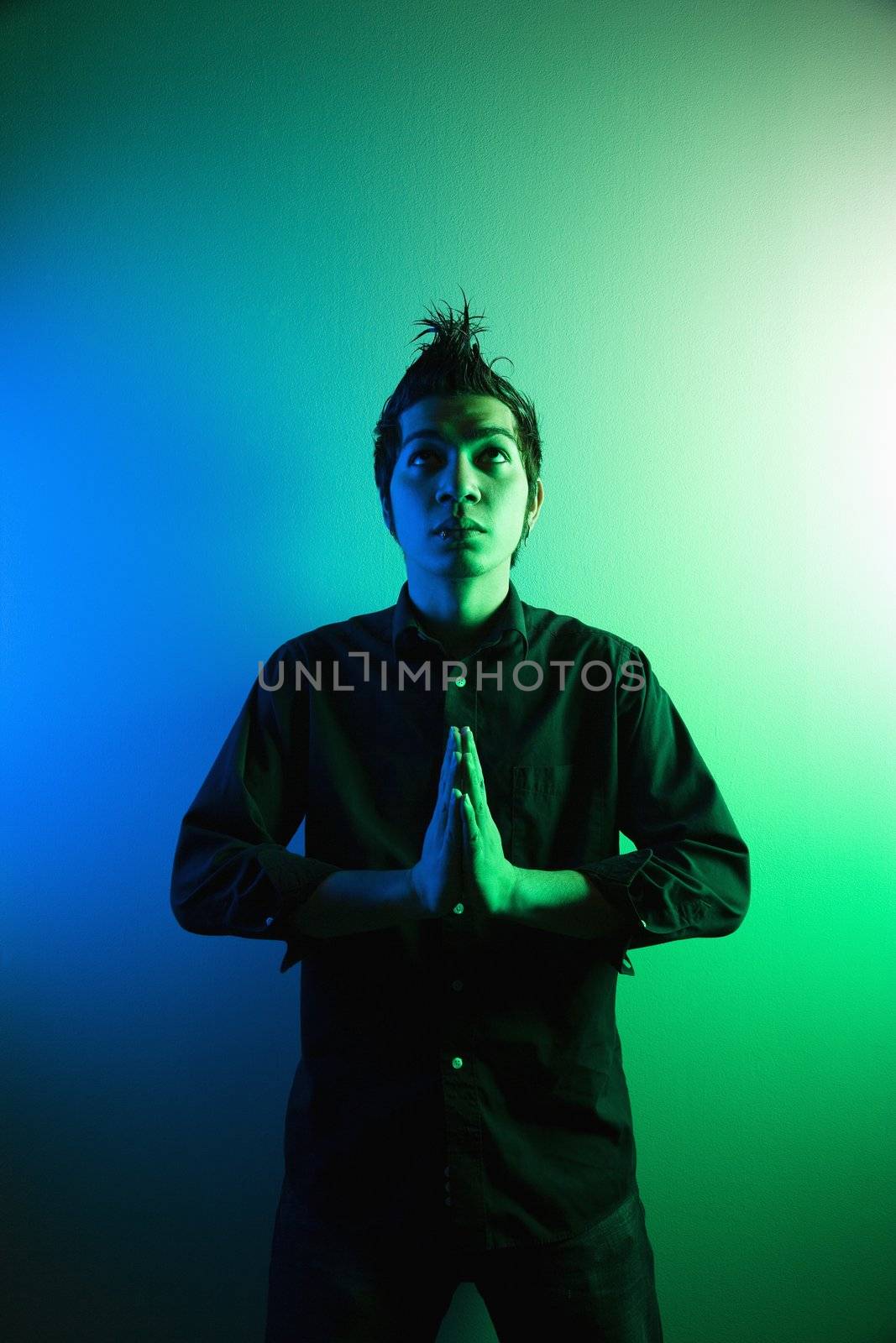 Portrait of attractive young Asian Filipino man standing holding hands in prayer position.