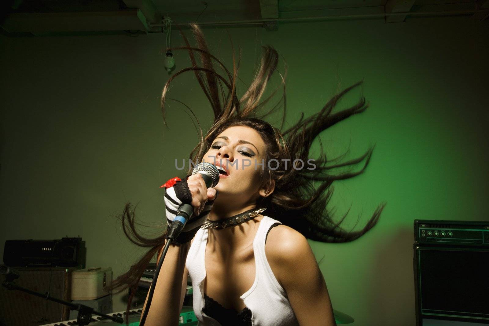 Caucasian female swinging head and hear while singing into microphone.