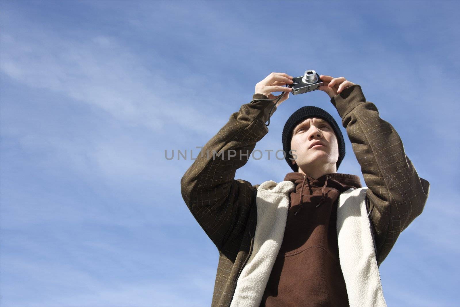 Caucasian male teenager taking a picture with a digital camera.