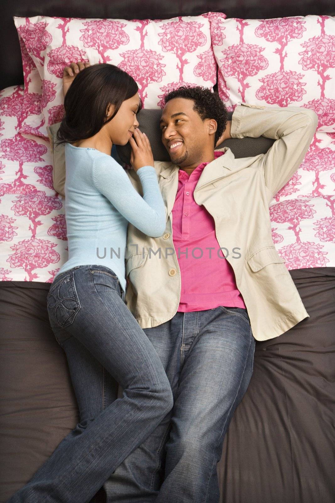 African American couple laying on bed looking at each other.