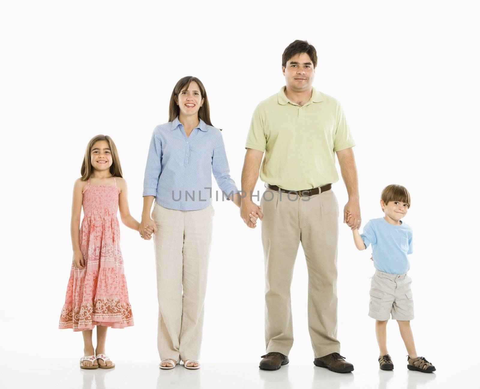 Hispanic family of four standing against white background holding hands.