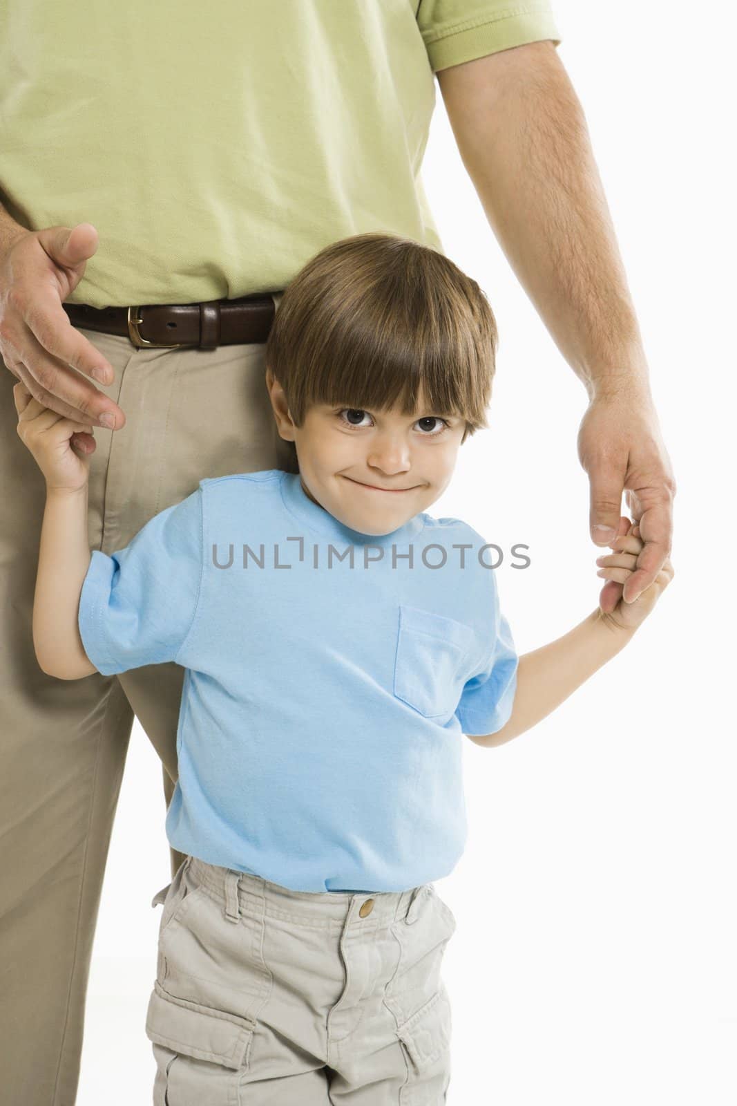 Boy holding onto father's hands standing against white background.