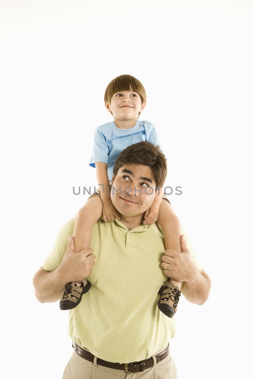 Father holding son on shoulders standing against white background.