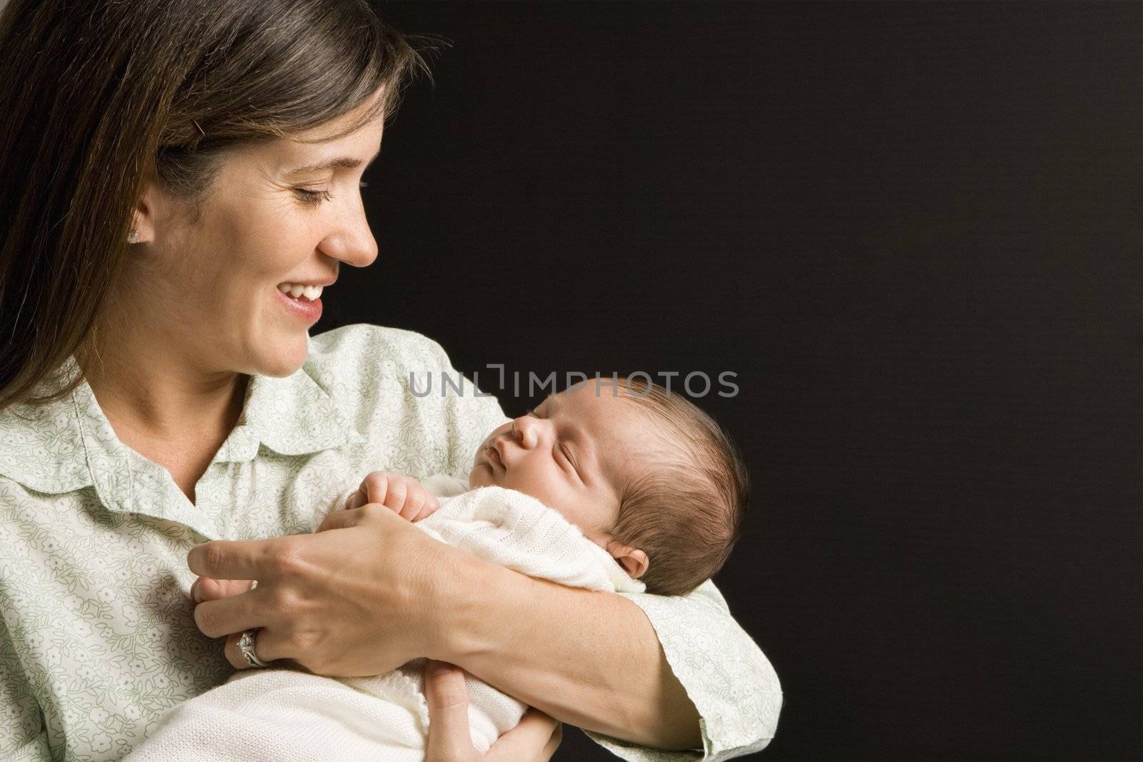 Mother smiling holding sleeping baby against black background.