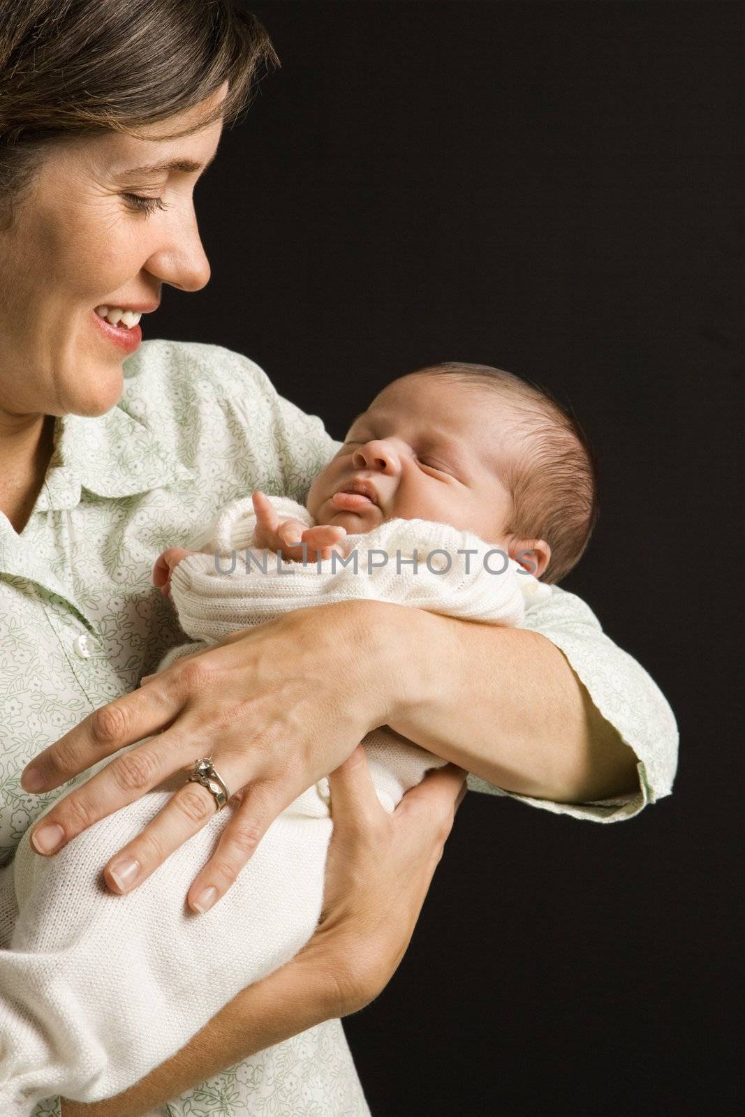 Mother smiling holding baby against black background.