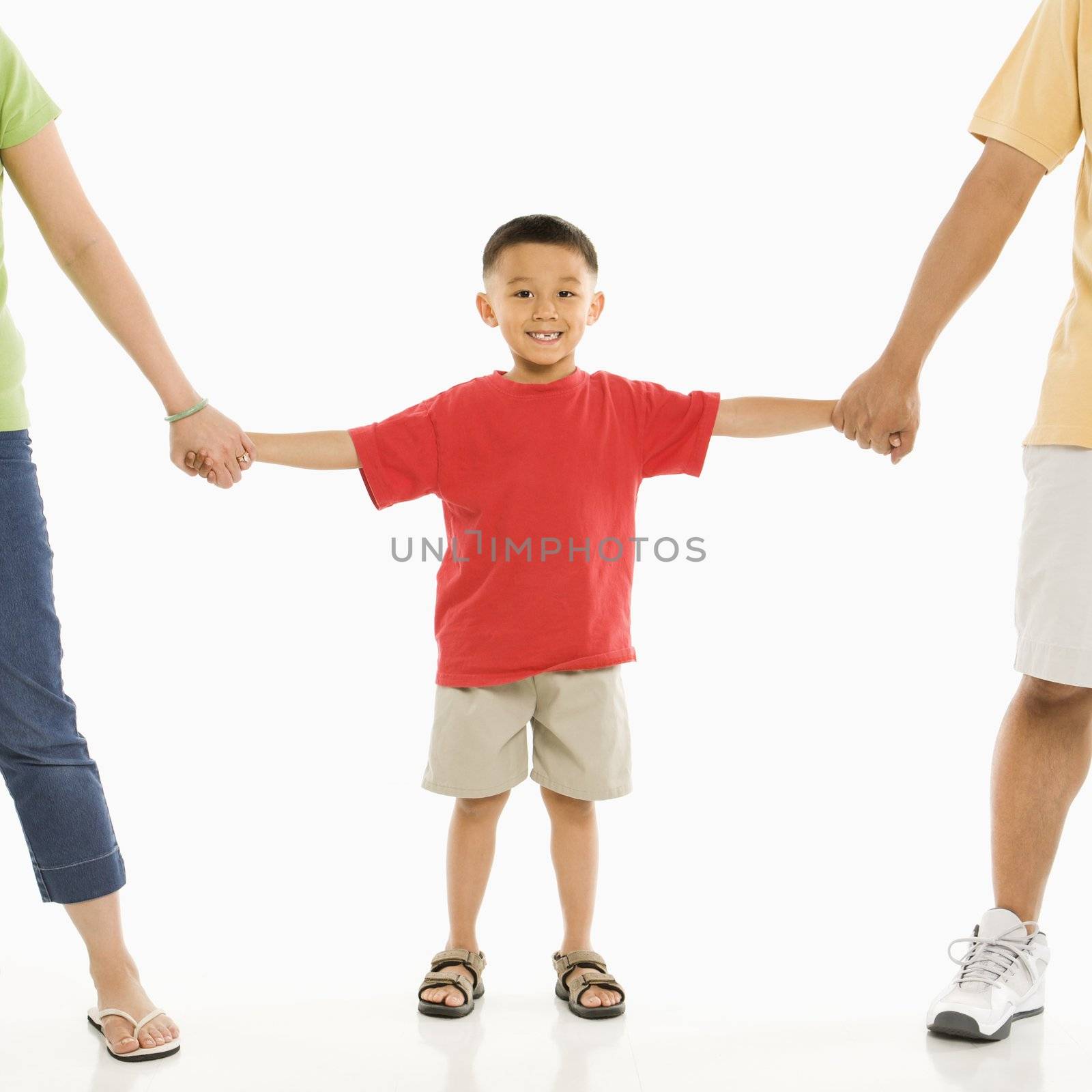 Asian parents holding hands with son in front of white background.