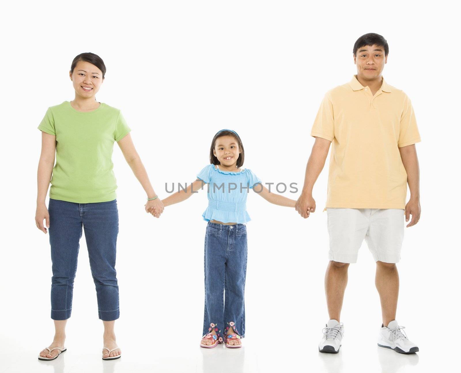 Asian parents holding hands with daughter in front of white background.