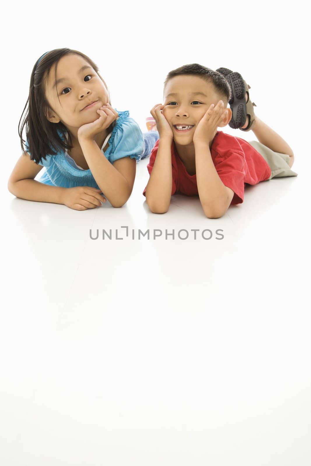 Asian brother and sister lying on floor with heads on hands.