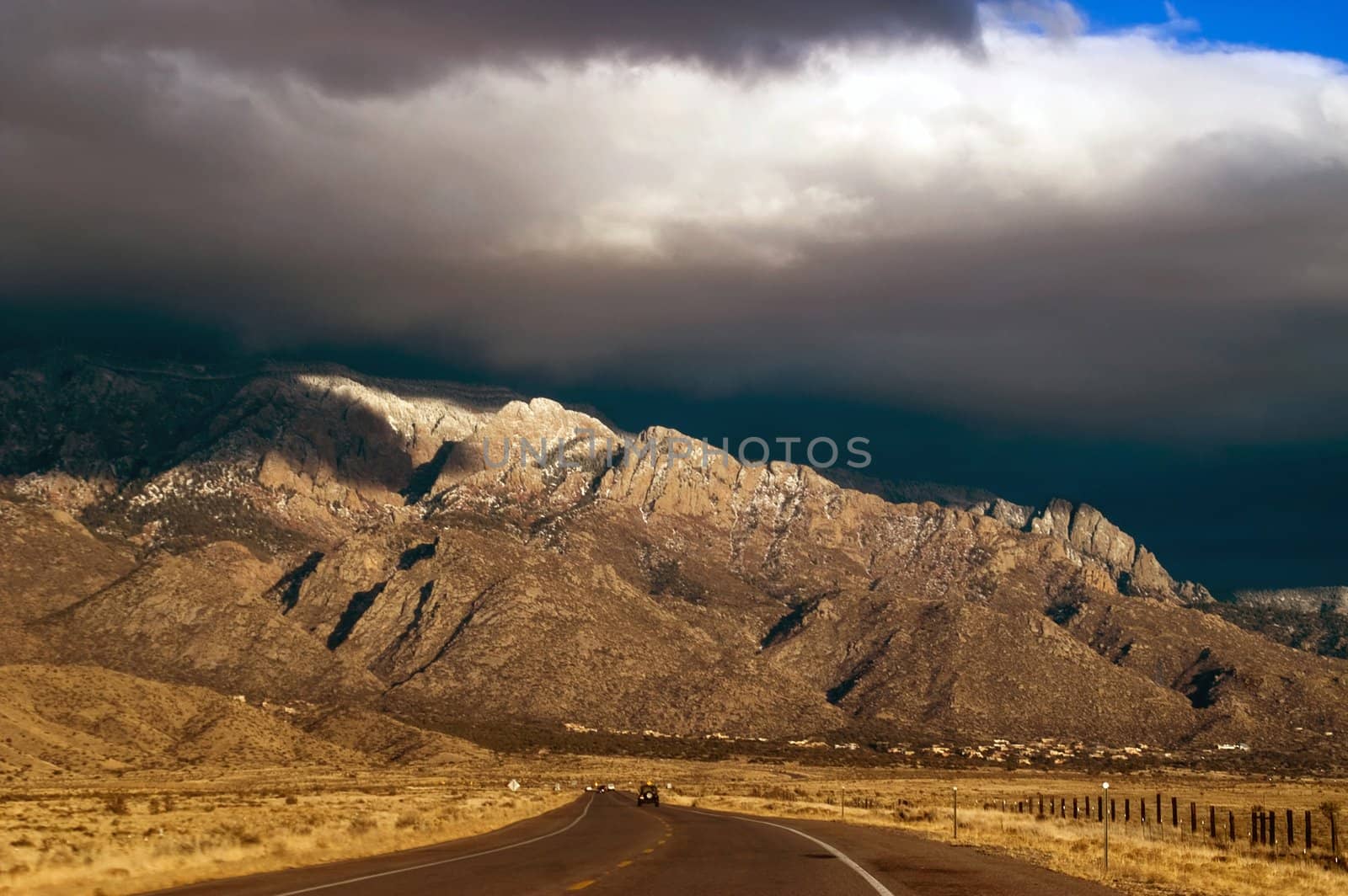 A highway in New Mexico showing the Sandia Mountains seems to lead to the awaiting thunderstorms in evening light just before sunset