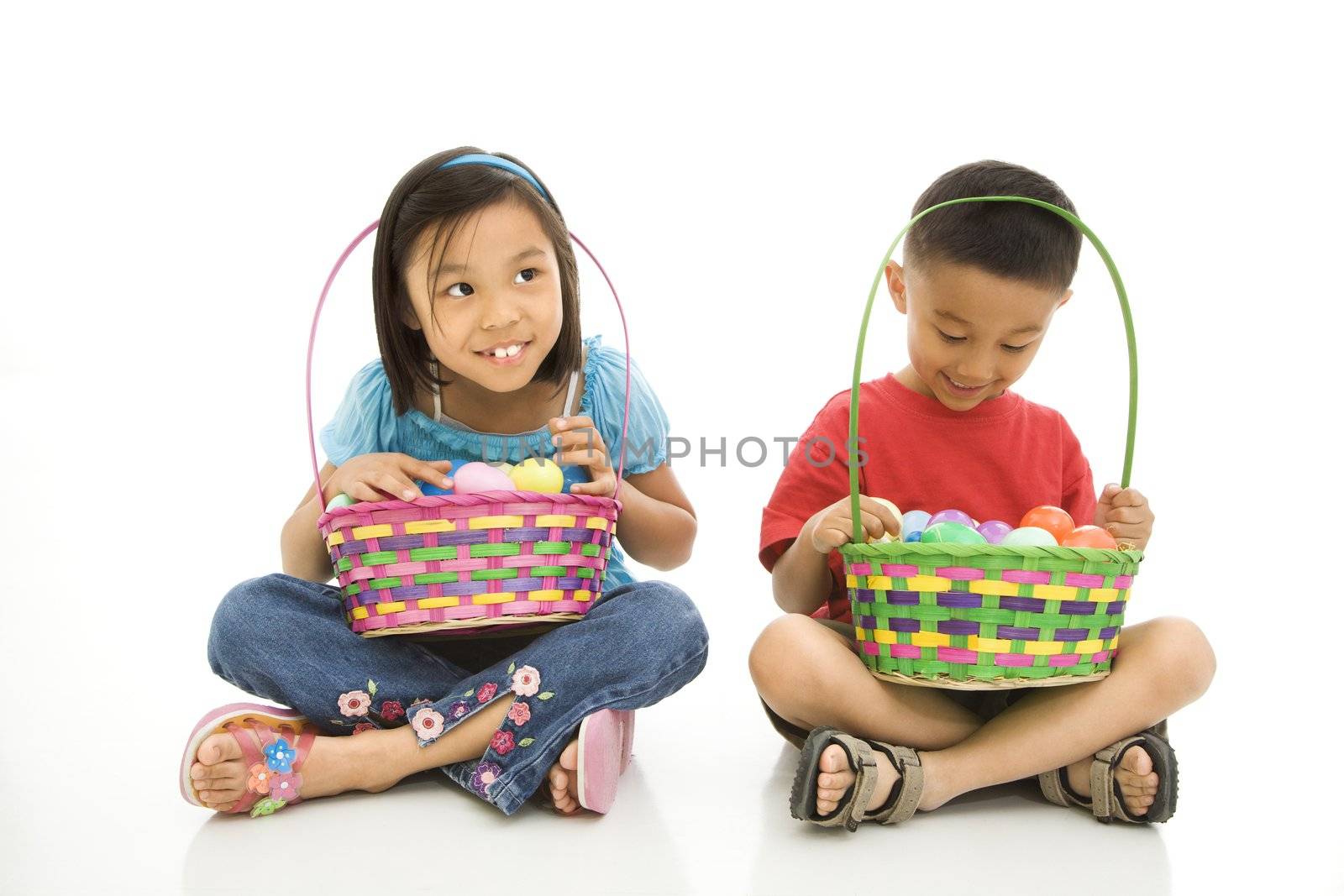 Asian girl and boy sitting on floor holding Easter baskets full of eggs.