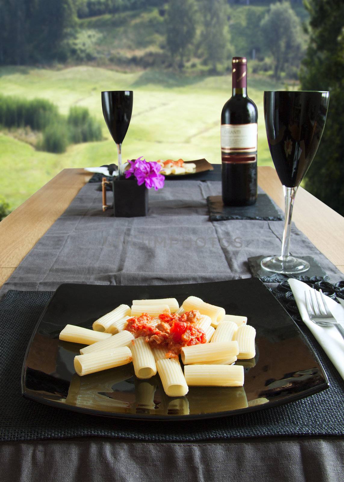 Table spread with Italian maccheroni over black plate, with green environment on the background
